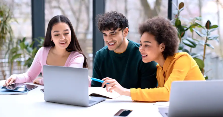 Engaged in a Digital Storytelling In Education project, a group of three students sitting at a desk in a coworking space and using a laptop.